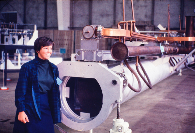 Peggy Hellweg in 1969 standing next to segment of the electron accelerator from the Stanford Linear Accelerator.