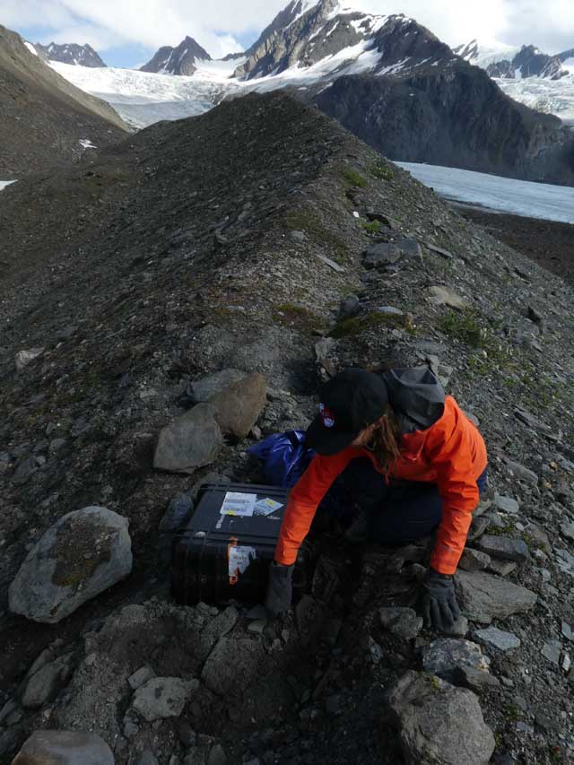 Researcher placing a seismic station on mountain ridge in Alaska